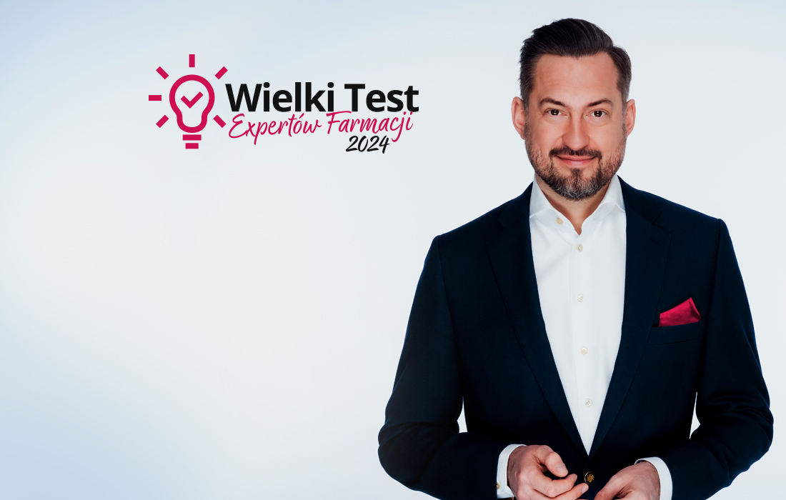 Mężczyzna w ciemnym garniturze z różową poszetką stoi obok logo Wielkiego Testu Ekspertów Farmacji 2024 na jasnym tle.