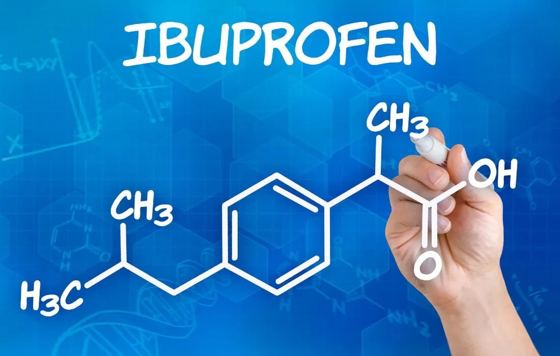 Ręka rysuje białą czcionką na niebieskim tle strukturę chemiczną ibuprofenu, u góry napis IBUPROFEN.