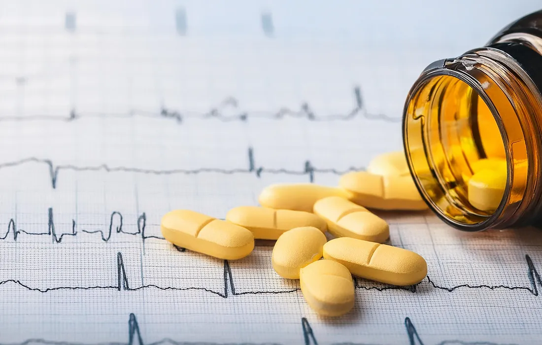 Bursztynowa butelka na tabletki przewróciła się, a żółte tabletki wysypały się na wydruk elektrokardiogramu (EKG) z widocznymi liniami rytmu serca.