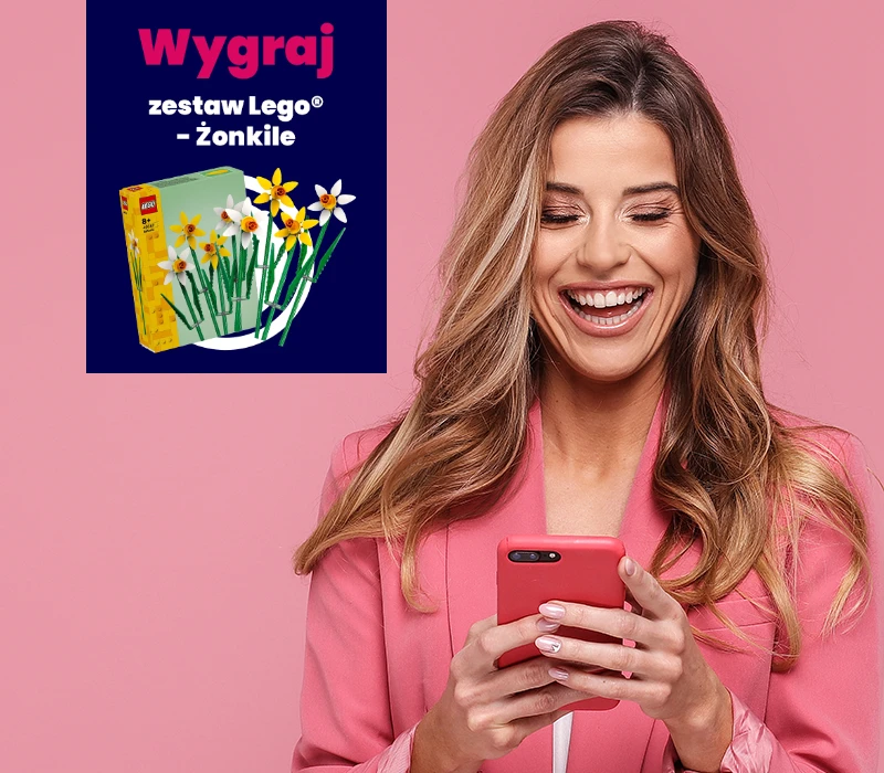 Uśmiechnięta kobieta w różowym blezerze patrzy na swój telefon. W rogu znajduje się grafika przedstawiająca zestaw LEGO Daffodil i polski tekst: Wygraj zestaw Lego Żonkile.