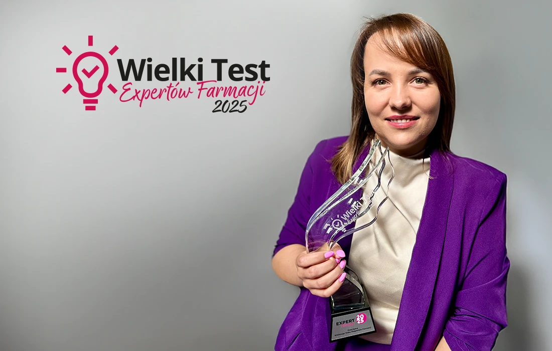 Kobieta w fioletowym blezerze trzyma szklane trofeum i się uśmiecha. Za nią znajduje się logo Wielki Test Ekspertow Farmacji 2025 z grafiką żarówki.