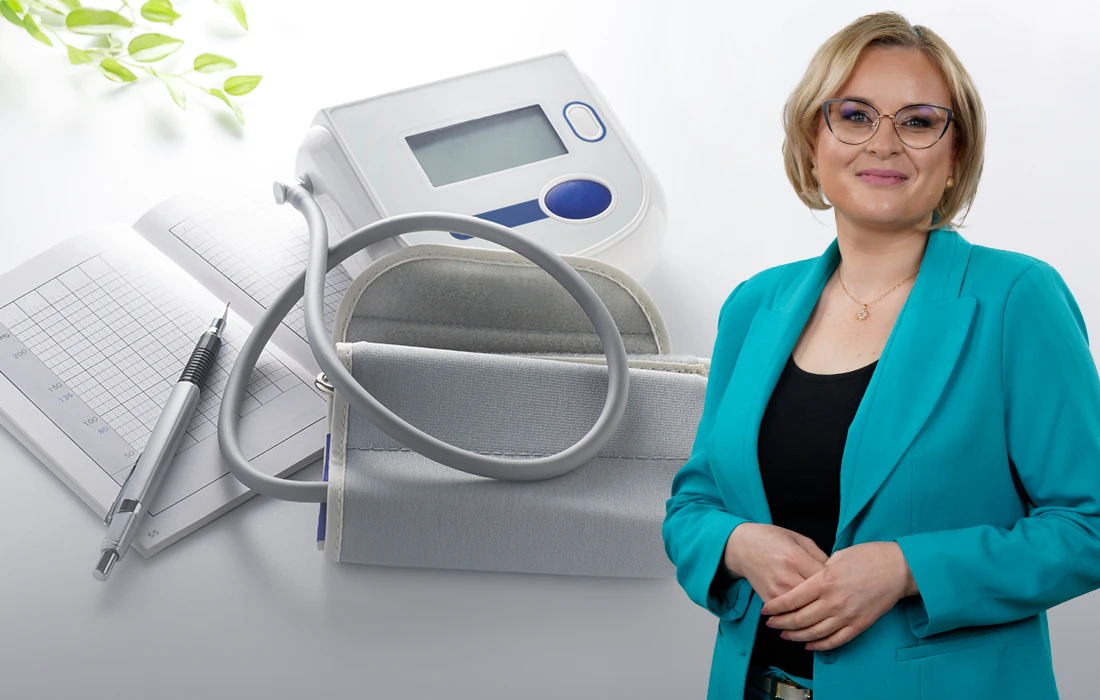 Uśmiechnięta kobieta w turkusowej marynarce stoi obok ciśnieniomierza, długopisu i karty zdrowia na białym tle z zielonymi liśćmi.