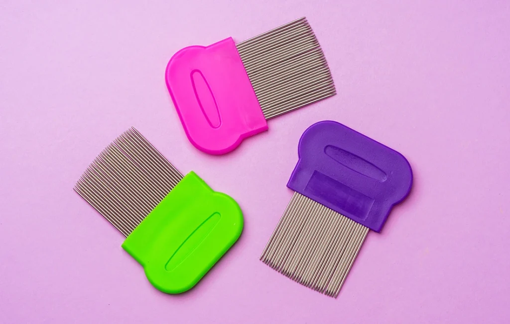 Trzy grzebienie na wszy o drobnych ząbkach z kolorowymi plastikowymi uchwytami - różowym, zielonym i fioletowym - są ułożone na jasnofioletowym tle.