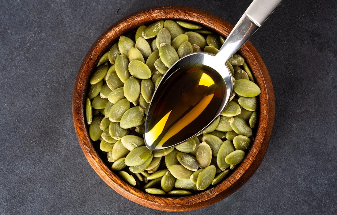 Drewniana miska wypełniona zielonymi pestkami dyni, z metalową łyżką spoczywającą na górze, zawierającą złoty olej z pestek dyni.