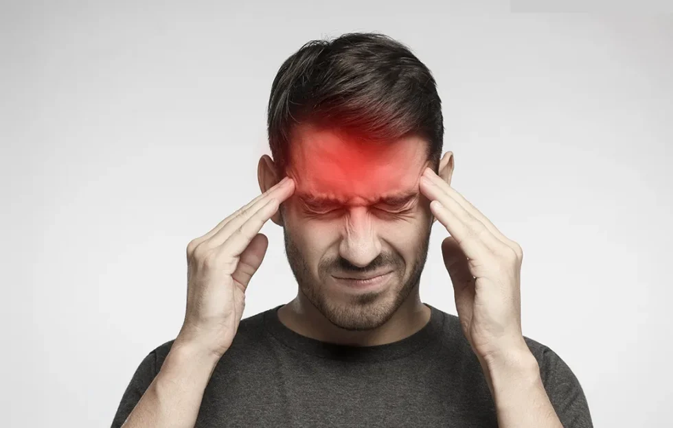 Mężczyzna dotyka skroni obiema rękami, z zamkniętymi z bólu oczami i czerwonym obszarem na czole, wskazującym na ból głowy.