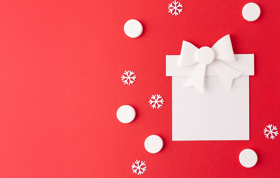 Pudełko upominkowe z białego papieru z kokardą na czerwonym tle, otoczone białymi tabliczkami i wyciętymi płatkami śniegu.