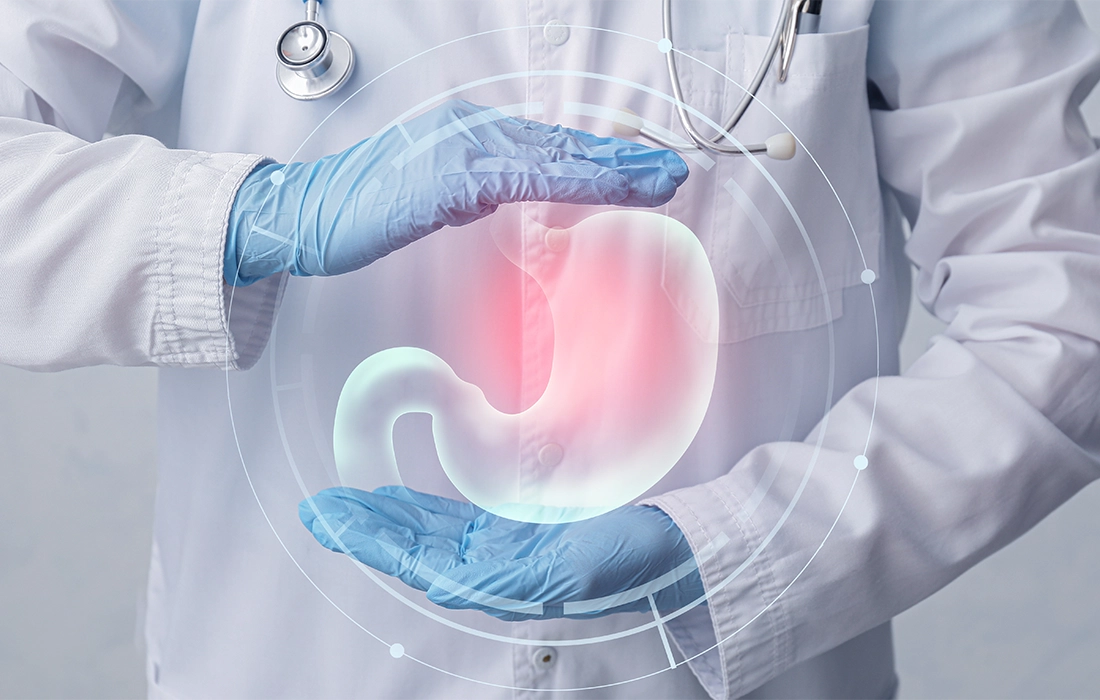 Lekarz w białym fartuchu i niebieskich rękawiczkach trzyma cyfrową ilustrację ludzkiego żołądka, podkreślając czerwony obszar wskazujący na ból lub dyskomfort.
