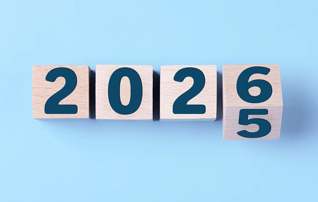 Cztery drewniane klocki na jasnoniebieskim tle pokazują liczby 2025, a ostatni klocek jest obracany, aby wyświetlić 2026.