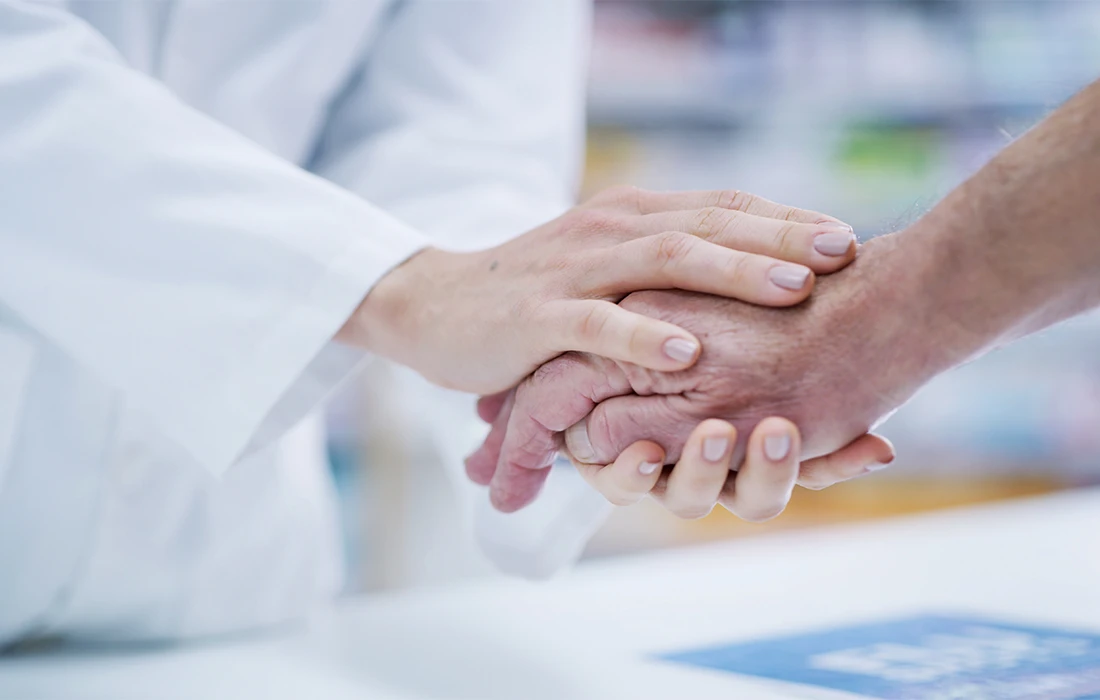 Osoba w białym fartuchu delikatnie trzyma dłoń innej osoby, przekazując wsparcie i współczucie w środowisku medycznym lub opieki zdrowotnej.