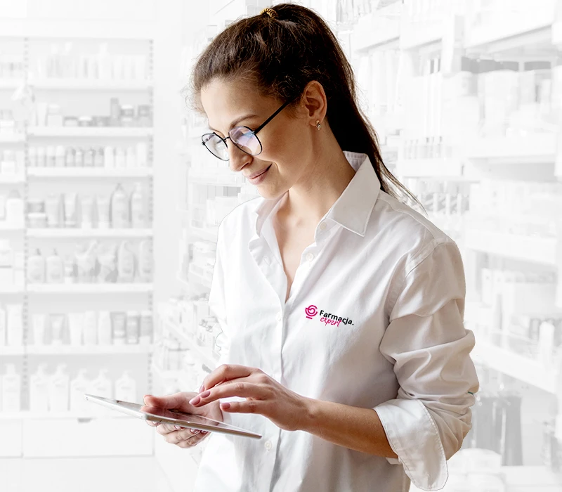 Farmaceutka w białej koszuli z logo 'Farmacja Expert' obsługuje tablet w nowoczesnej aptece.